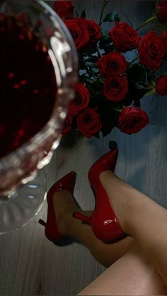 a woman's legs with red shoes next to a glass of wine and roses