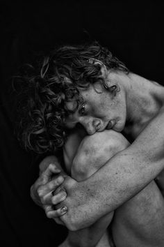 black and white photograph of a naked man with his head on his hands, looking down