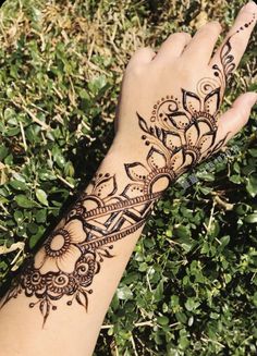 a henna tattoo on someone's hand with green grass and bushes in the background