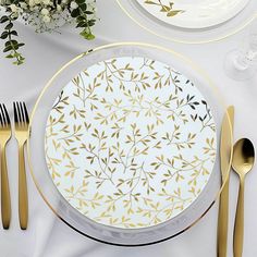 a white and gold table setting with plates, silverware and flowers on the table