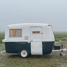 an old camper trailer parked in a field on a foggy day