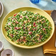 a yellow bowl filled with peas on top of a table next to plates and silverware