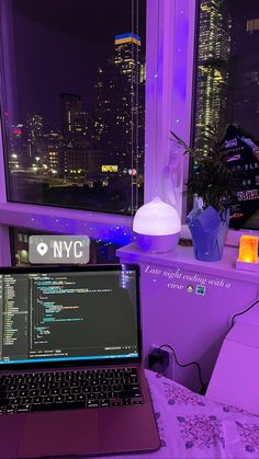 a laptop computer sitting on top of a bed in front of a window at night