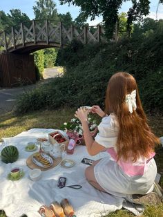 a woman sitting on top of a blanket next to a picnic table filled with food