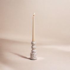 a white candle sitting on top of two stacked rocks in front of a beige background