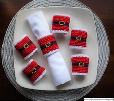 four crocheted santa claus napkin holders on a white plate with silver trimmings