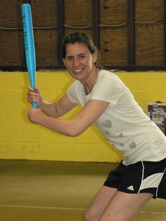 a woman holding a blue baseball bat on top of a hard wood floor in a gym