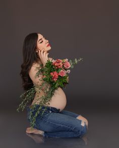 a pregnant woman sitting on the floor with flowers in her hand and looking up at something