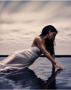 a woman in a white dress sitting on the water