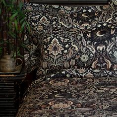 a bed covered in black and white floral print pillows next to a potted plant