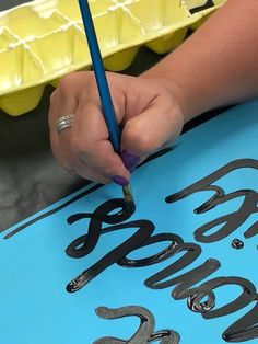 a person is writing on a piece of paper with a blue pen and yellow container in the background