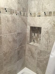 a bathroom with marble tile walls and flooring in the shower area, along with a white bathtub