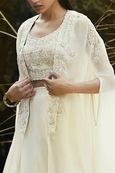 Ivory cape with embroidered floral motifs with pearl, sequin and cutdana embellishments. Comes with padded inner blouse and can can attached solid lehenga skirt. - Aza Fashions Beige Choli With Sheer Dupatta, Elegant Cape Sleeve Tops For Wedding, Elegant Tops With Cape Sleeves For Wedding, Elegant Wedding Tops With Cape Sleeves, Anarkali Sharara For Ceremonies, Anarkali Tops With Dupatta For Wedding, Off White Anarkali Set For Party, Cream Fitted Set With Sheer Dupatta, Cream Fitted Sets With Sheer Dupatta