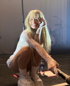 a woman with long blonde hair and white boots is sitting on the floor in front of a microphone