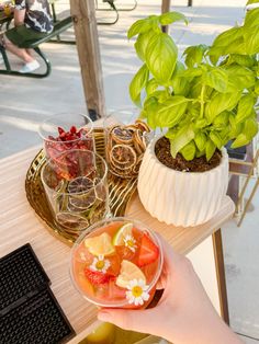 a person is holding a bowl of fruit on a table with other food and drinks