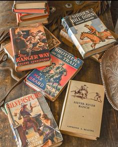 several books are sitting on top of a wooden table next to an old western hat