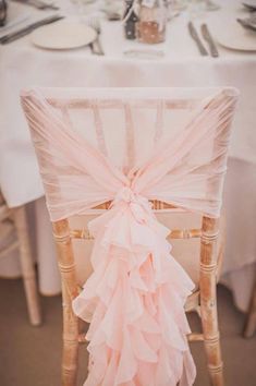 the back of a chair covered in pink ruffles at a table with plates and silverware