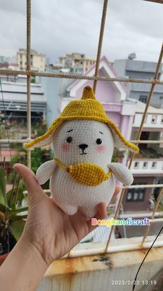 a hand holding a small white stuffed animal with a yellow hat on it's head