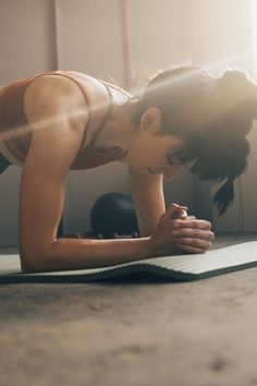 a woman is doing push ups on her yoga mat in the sunbeams,