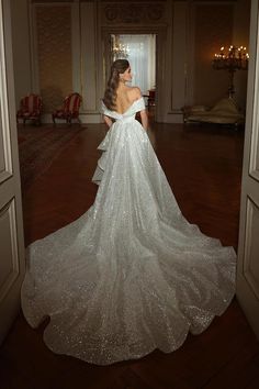 a woman in a white wedding dress is looking at herself through an open door to another room