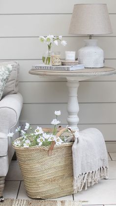 a basket filled with flowers next to a white chair and lamp on top of a table