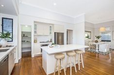 a large kitchen with white cabinets and wooden flooring is pictured in this image, there are three stools at the center of the island