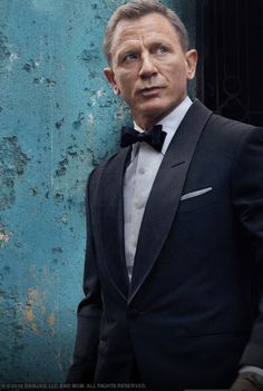 a man in a tuxedo standing next to a blue wall