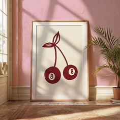 a framed poster with two cherries hanging on the wall next to a potted plant