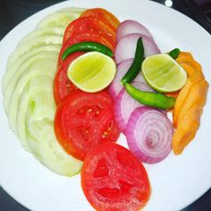 sliced vegetables on a white plate with limes, onions, and red onion wedges