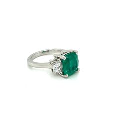 This Elegant Platinum three stone ring has a Natural Cushion Cut Colombian Emerald from the Top Muzo Mine with a GIA Certificate. The side stones are Natural Brilliant Cut Trapezoid Pair of Matching Diamonds. GIA#5202111099 3.34 Carat Cushion Modified 9.64x8.93x5.64 with moderate F2 clarity enchancement. 2 Matching Trapezoid Brilliant Cut Diamonds weigh 0.71 carats total weight and are graded G in color and SI1 to SI2 in clarity. Platinum weight is 5.14 DWT. Ring can be sized. UNBEATABLE PRICE!! Three Stone Diamond Gemstones For Anniversary, Luxury Three Stone Gemstones For Anniversary, Luxury Three Stone Emerald Ring For Formal Occasions, Luxury Three Stone Emerald Ring, Luxury Three Stone Emerald Ring For Formal Events, Luxury Emerald Three Stone Ring For Formal Occasions, Three Stone Diamond Gemstones For Wedding, Formal Three Stone Emerald Ring In Fine Jewelry Style, Timeless Three Stone Emerald Ring For Formal Occasions