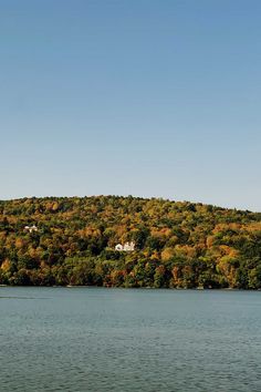 a large body of water surrounded by trees with fall colors on the hills in the background