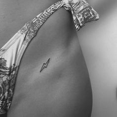 a black and white photo of a woman's stomach with a small arrow tattoo on it