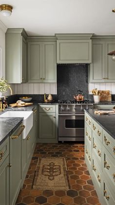 a kitchen with green cabinets and black counter tops, an oven, sink, and stools