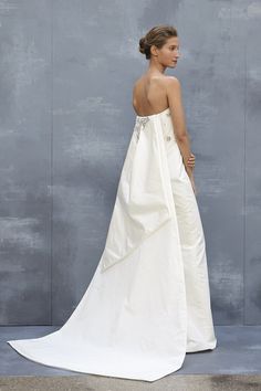 a woman in a white wedding dress standing against a gray wall with her back to the camera