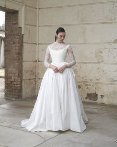 a woman in a white wedding dress is standing on the floor with her hands behind her back