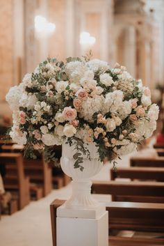 a vase filled with white and pink flowers on top of a wooden table next to pews