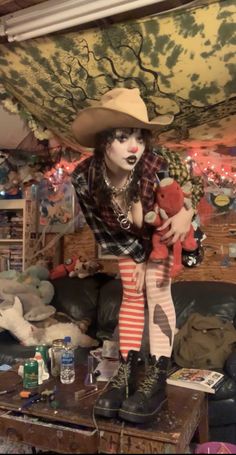 a woman dressed as a scarecrow holding a teddy bear in a living room filled with toys