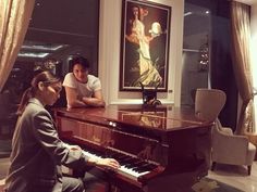 two people sitting at a piano in front of a painting