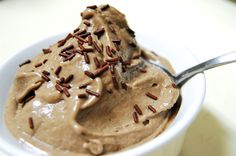 a spoon full of chocolate ice cream with sprinkles on top and in a white cup