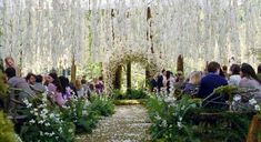 people are sitting in chairs at the end of an aisle with flowers hanging from it