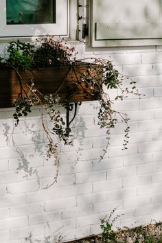 a window box with plants growing out of it on the side of a white brick building