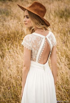 a woman in a white dress and brown hat is standing in tall grass with her back to the camera