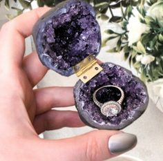 a person holding a ring in their hand next to a purple stone with a diamond on it