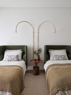 two beds with green headboards in a white walled room, one is made up and the other has pillows on it