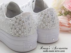 a pair of white shoes with pearls on the side and flowers in the back ground