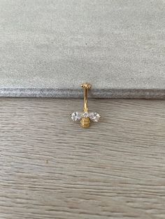 a yellow gold nose piercing with three small white stones on the top and bottom, sitting on a wooden surface