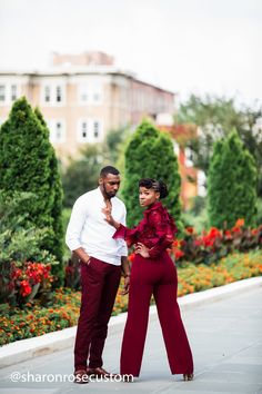 a man and woman standing next to each other in front of some flowers on the sidewalk