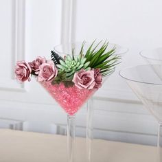 two martini glasses with flowers and succulents in them on a table next to each other