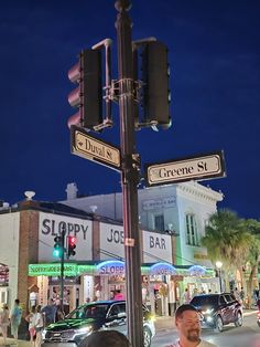 people are standing on the sidewalk at night in front of shops and stores with street signs