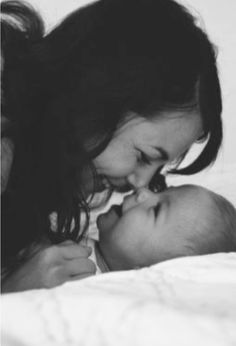 a woman is kissing her baby on the cheek while laying in bed with it's mother